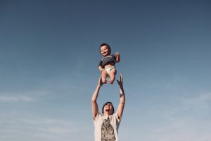Man raising his baby under blue sky.
